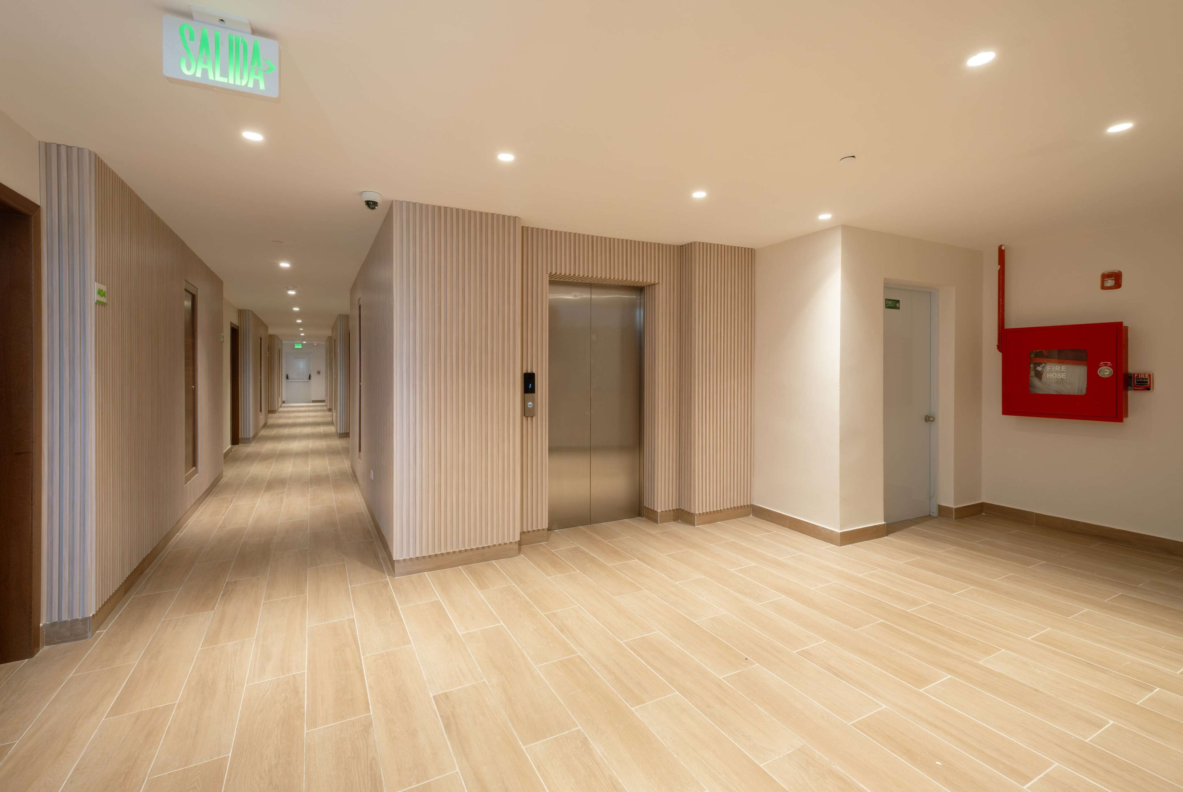 A hotel corridor with a tiled floor, an elevator, and a fire extinguisher on the wall.