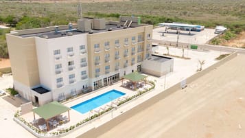 Un hotel de varios pisos con piscina en la azotea, zona de estar al aire libre y una estación de servicio al fondo.