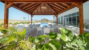 An outdoor pool area with a wooden pergola, white lounge chairs, and a pool table.