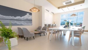 A modern dining area with a large table and multiple chairs, a painting on the wall, and a potted plant.