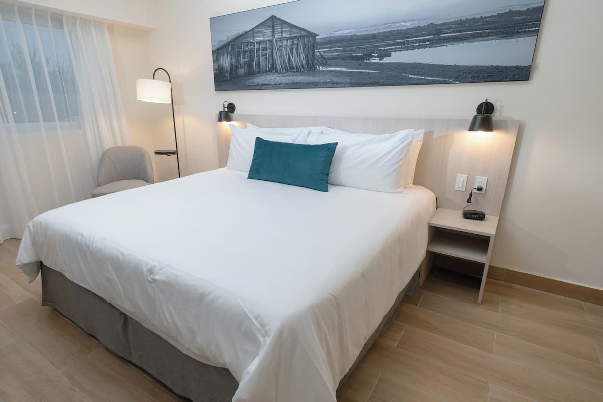 Ein Hotelzimmer mit einem großen Bett, einem Nachttisch, einem Sessel, einer Lampe und einem Bild an der Wand.