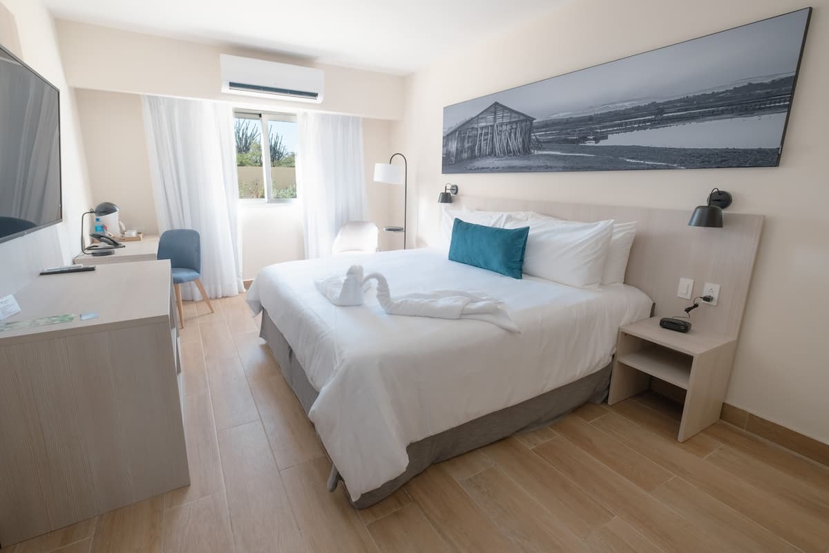 Ein Hotelzimmer mit Bett, Schreibtisch, Stuhl, Nachttisch und einem an der Wand befestigten Fernseher.