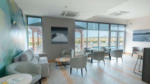 A modern hotel lobby with a seating area, large windows, and a view of the pool.