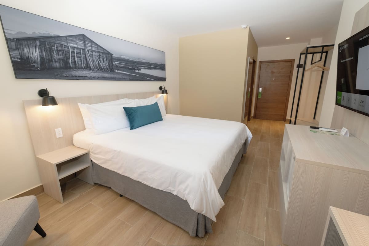 Ein modernes Hotelzimmer mit einem großen Bett, einem Nachttisch, einem Schreibtisch und einem Fernseher.