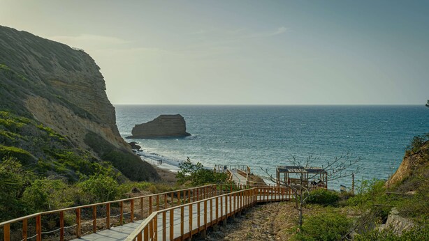 A coastal walkway with a wooden railing, leading to a rocky outcrop and the sea.