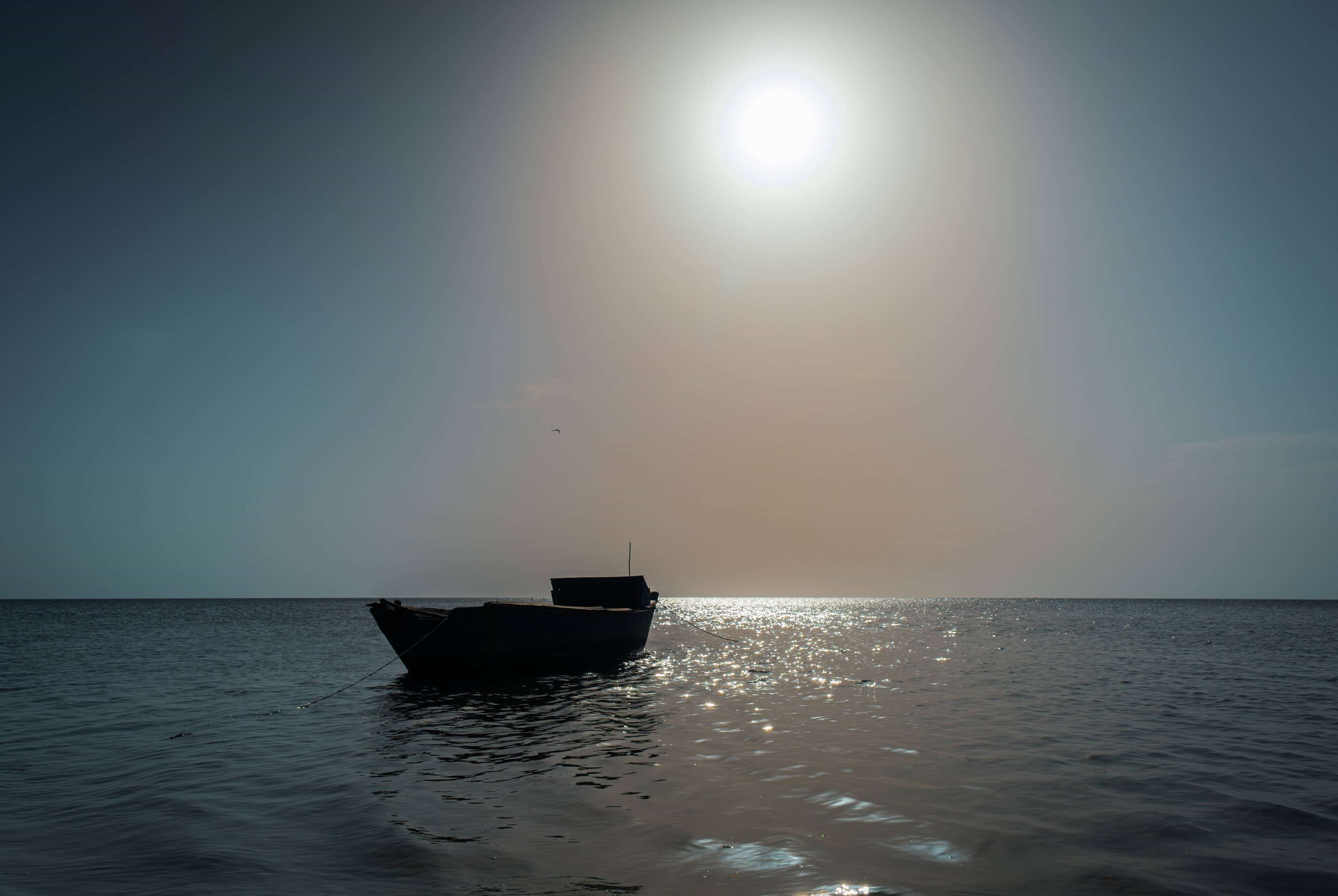 Un bateau est amarré dans des eaux calmes, sous un ciel dégagé et un soleil éclatant.