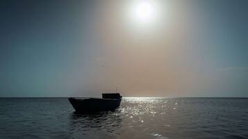 A boat anchored in calm waters with a clear sky and the sun shining brightly.