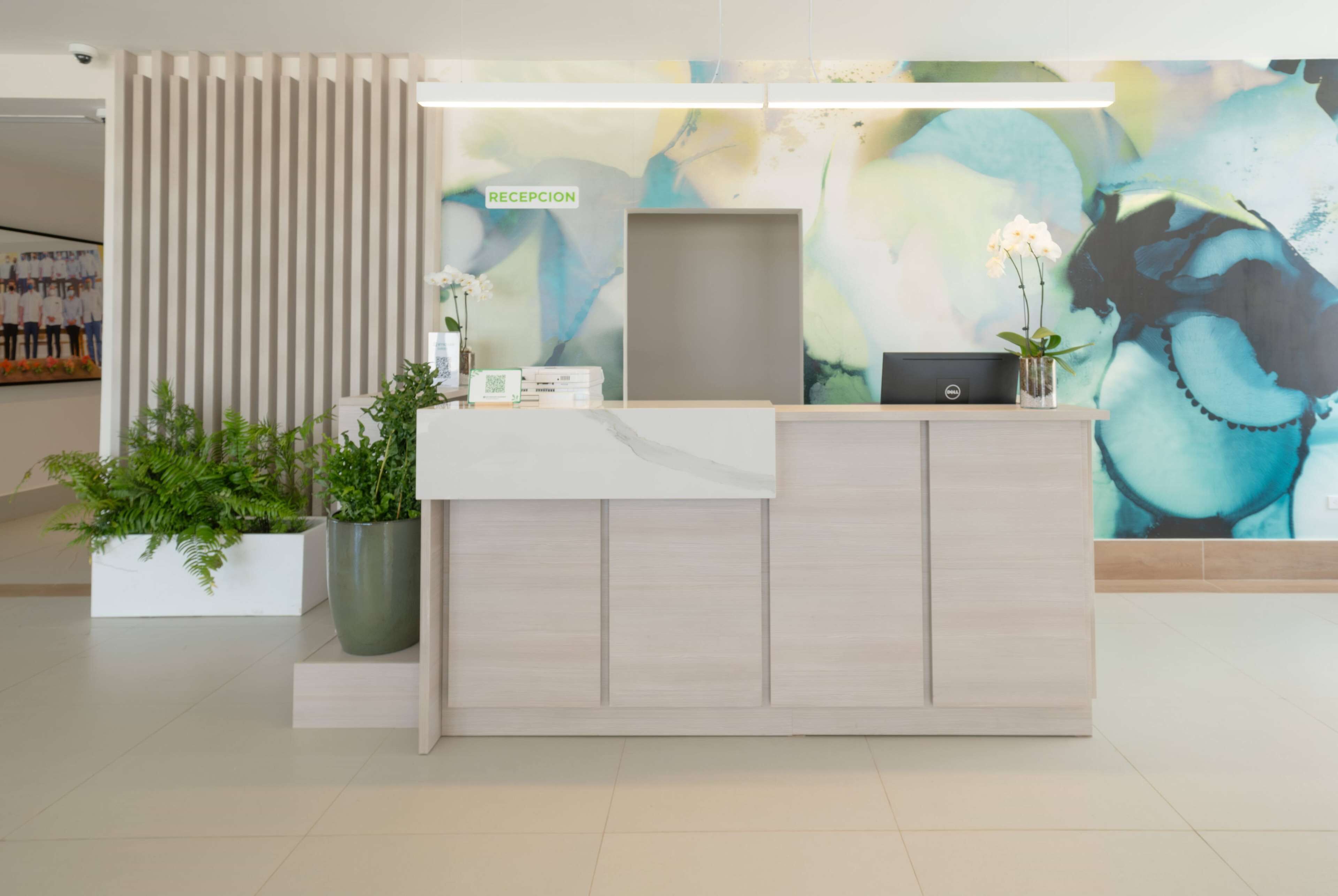 A reception desk with a modern design, a sign labeled "RECEPCION", and a large abstract painting on the wall.