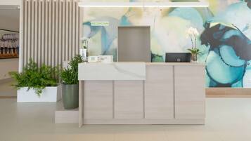 A reception desk with a modern design, a sign labeled "RECEPCION", and a large abstract painting on the wall.