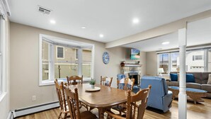 A dining area with a wooden table and chairs, a fireplace, a television, and a sofa in a living room. - Vacation rental with pool on LBI (Brant Beach)