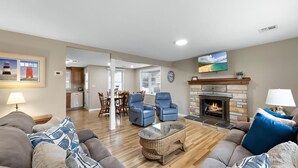 A living room with a fireplace, a dining area, and a kitchen in the background. - Vacation rental with pool on LBI (Brant Beach)