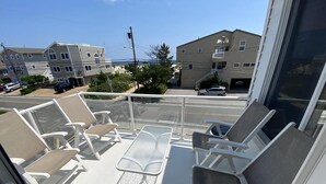 Un balcon avec des chaises blanches et une table, donnant sur une rue animée par la circulation des voitures et bordée d’immeubles.