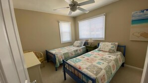 Une chambre avec deux lits, un ventilateur de plafond et deux fenêtres équipées de stores.