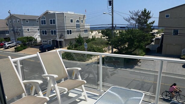 Un balcon avec des chaises blanches et une table en verre, donnant sur une rue animée par la circulation des voitures et bordée d’immeubles.