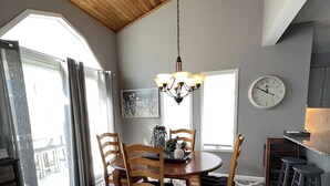 A dining area with a wooden table and chairs, a chandelier, a clock, and a view through a window. - Beautiful Townhome located near the beach in Beach Haven. (Beach Haven)