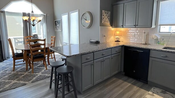 A modern kitchen with grey cabinets, a black dishwasher, and a dining area with wooden chairs and a table. - Beautiful Townhome located near the beach in Beach Haven. (Beach Haven)