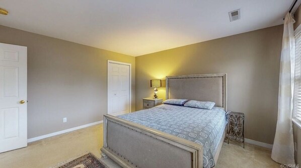 A bedroom with a bed, nightstands, a door, and a window with curtains.