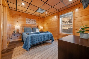 A cozy wooden room with a bed, bedside tables, a window, and a potted plant.
