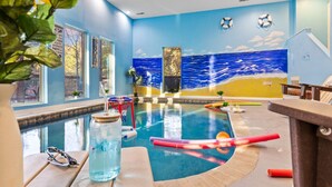 An indoor swimming pool with a blue and yellow mural, a basketball hoop, and a glass of water on a table.