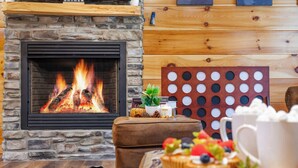 A cozy room with a stone fireplace, a wooden wall panel, a small table with a plant, a candle, and a decorative board.