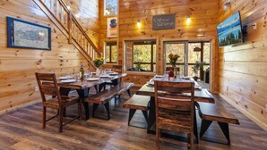 A wooden cabin interior with a dining area, wooden benches, and a staircase.