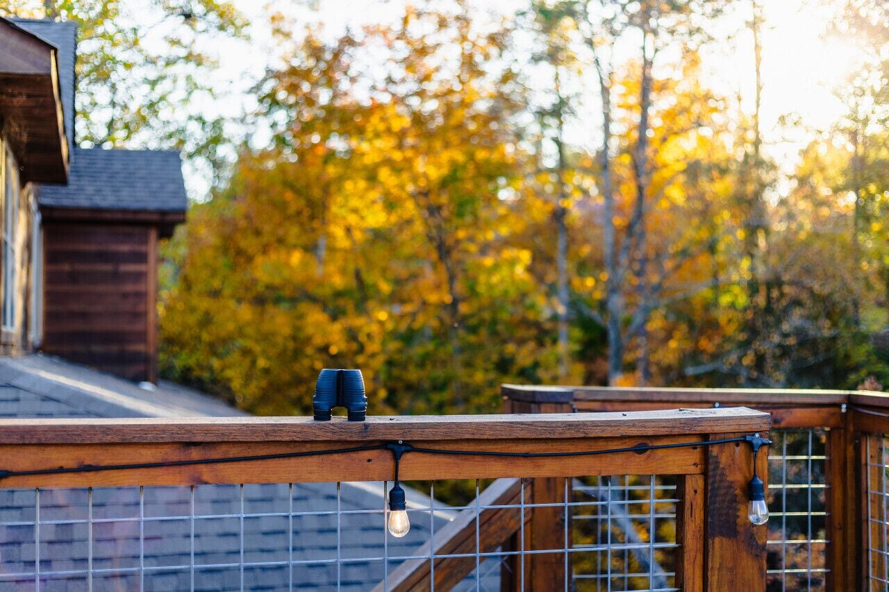 Una terraza de madera con barandilla, una lámpara y una mesita.
