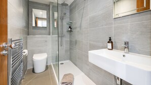 Un baño moderno con ducha de vidrio, lavamanos blanco y un inodoro.