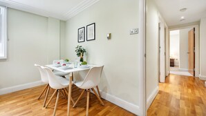 Un comedor con una mesa y sillas blancas, un jarrón con planta y cuadros en la pared.