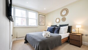 Un dormitorio con cama, mesitas de noche, un radiador, una ventana y decoración en la pared.