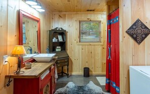 Een houten badkamer met een wastafel, spiegel en een rode kast.