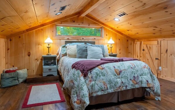 Un dormitorio de cabaña de madera acogedor, con una cama, dos mesitas de noche, un velador y una ventana, además de una alfombra roja.
