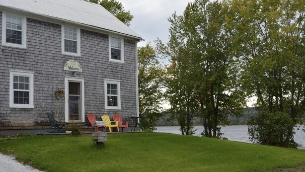 A two-story house with a 'Welcome' sign, a grassy yard, and a lake view.