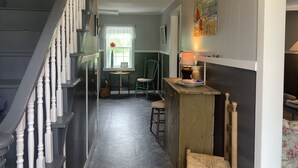 A narrow hallway with a staircase on the left, a window with a flower, a small table with a lamp, and a chair.