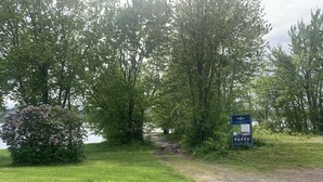 A park entrance with a signboard, a gravel path, and lush greenery.