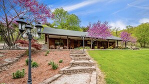 A log cabin with a covered porch, stone steps leading to the entrance, and a well-maintained lawn. - Secluded Hillside Cabin on Historic working Farm (Lampe)