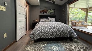 A bedroom with a bed, a ceiling fan, a nightstand, a lamp, and a window with a view of greenery. - Secluded Hillside Cabin on Historic working Farm (Lampe)