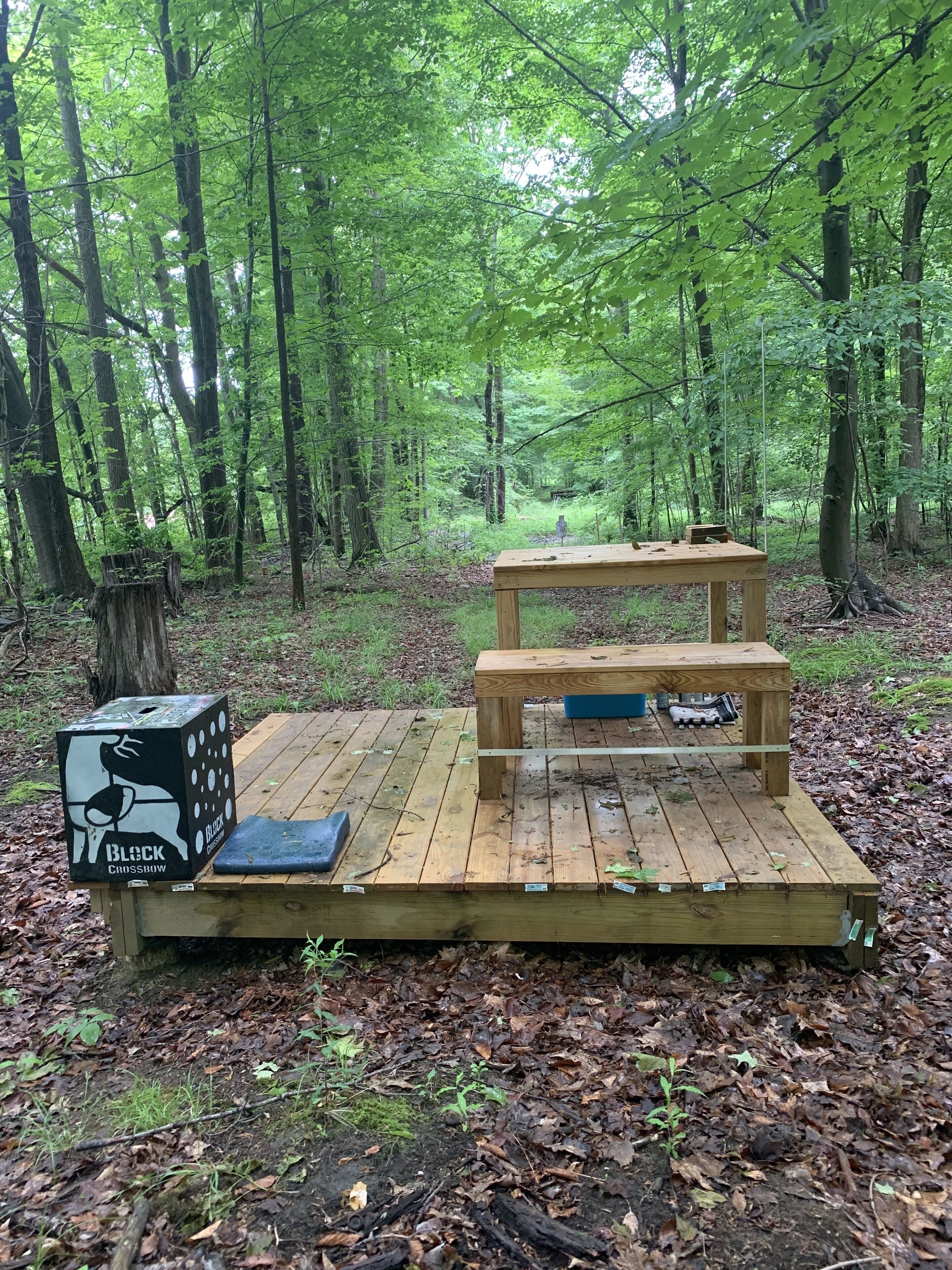 A wooden deck in a forest with a Black Crossbow box and a table.
