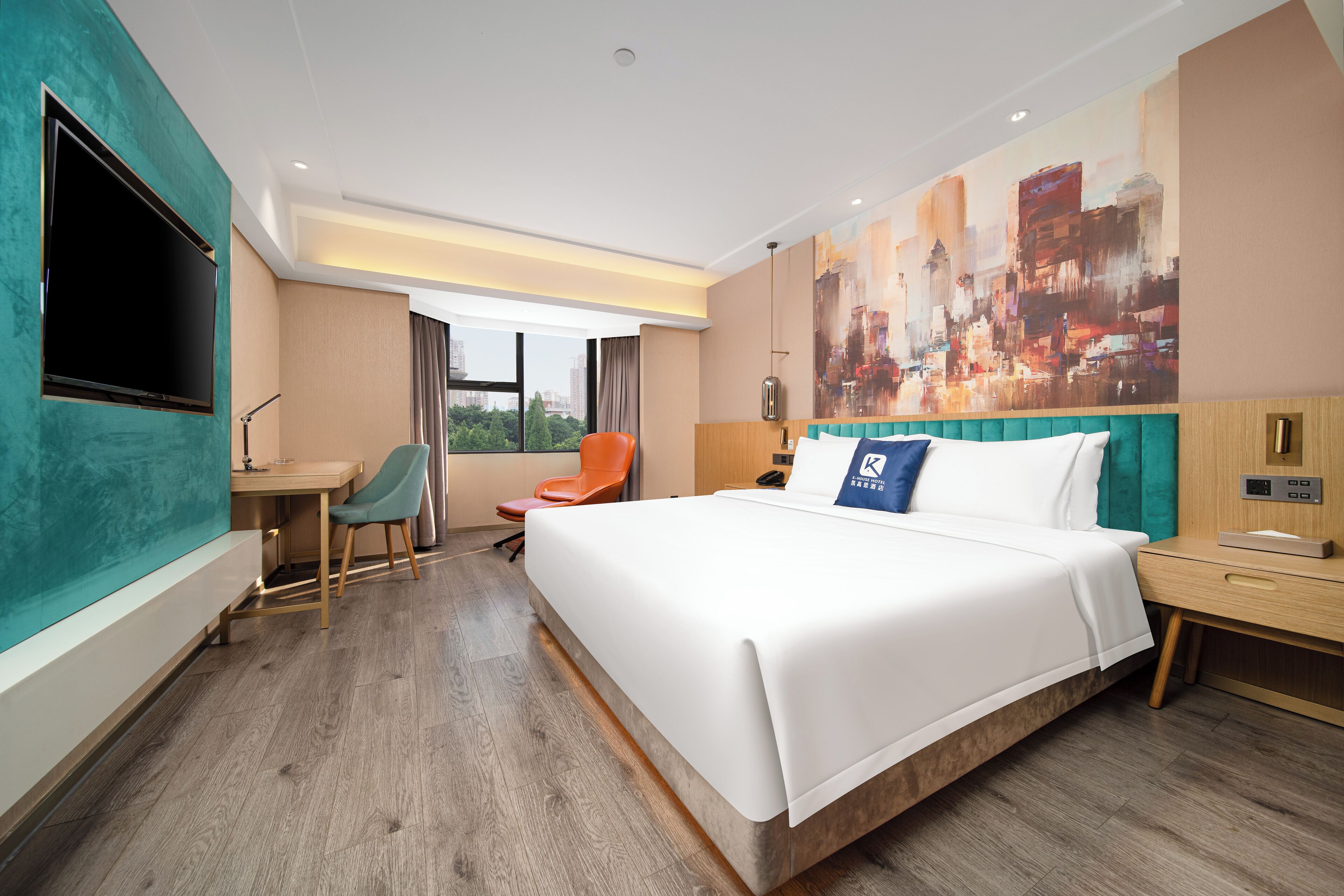 A modern hotel room with a large bed, a desk, a chair, a TV, and a cityscape painting on the wall.