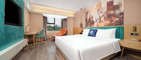 A modern hotel room with a large bed, a desk, a chair, a TV, and a cityscape painting on the wall.