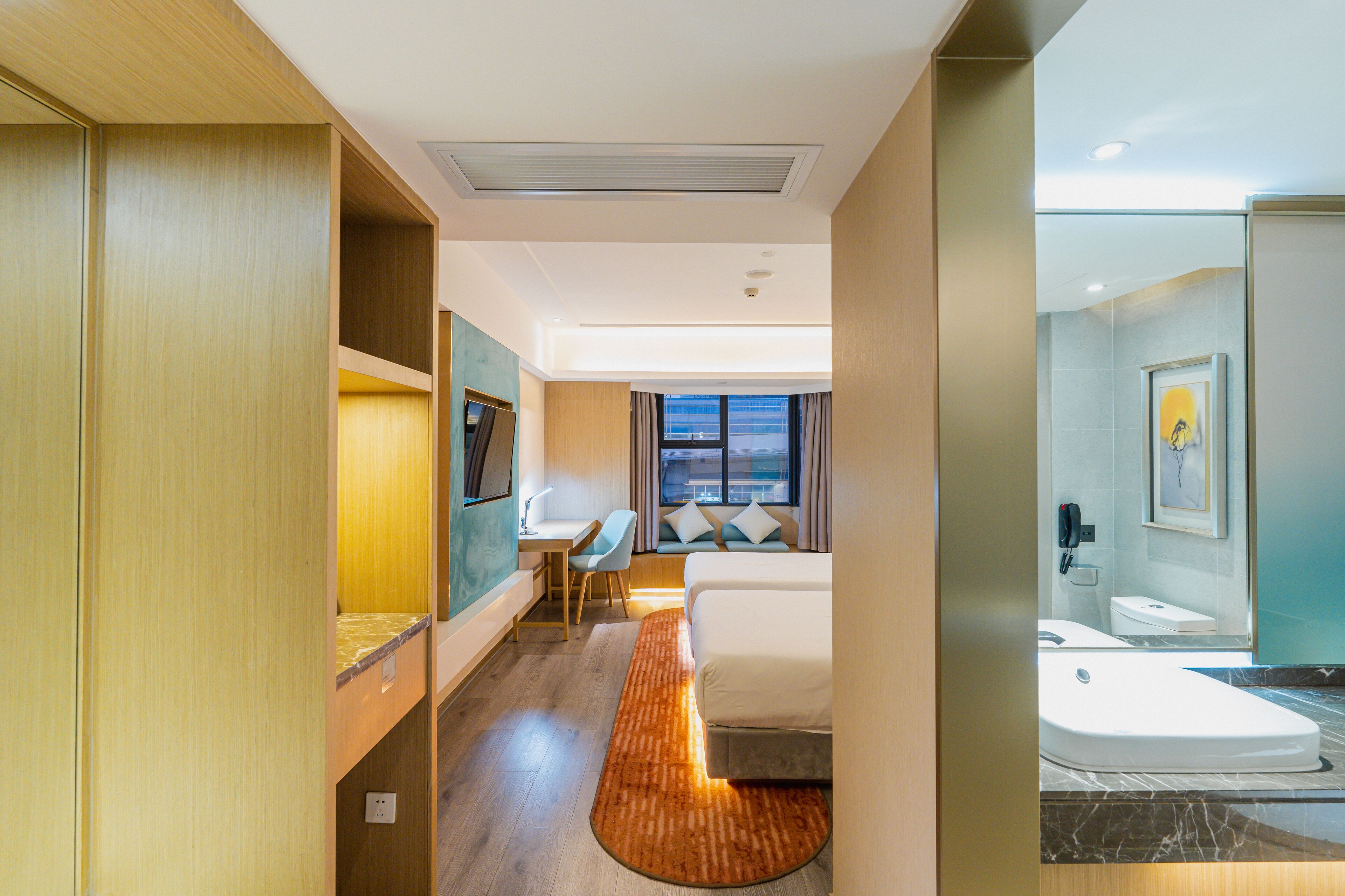 A hotel room with a bed, desk, chair, and a bathroom with a toilet and sink.