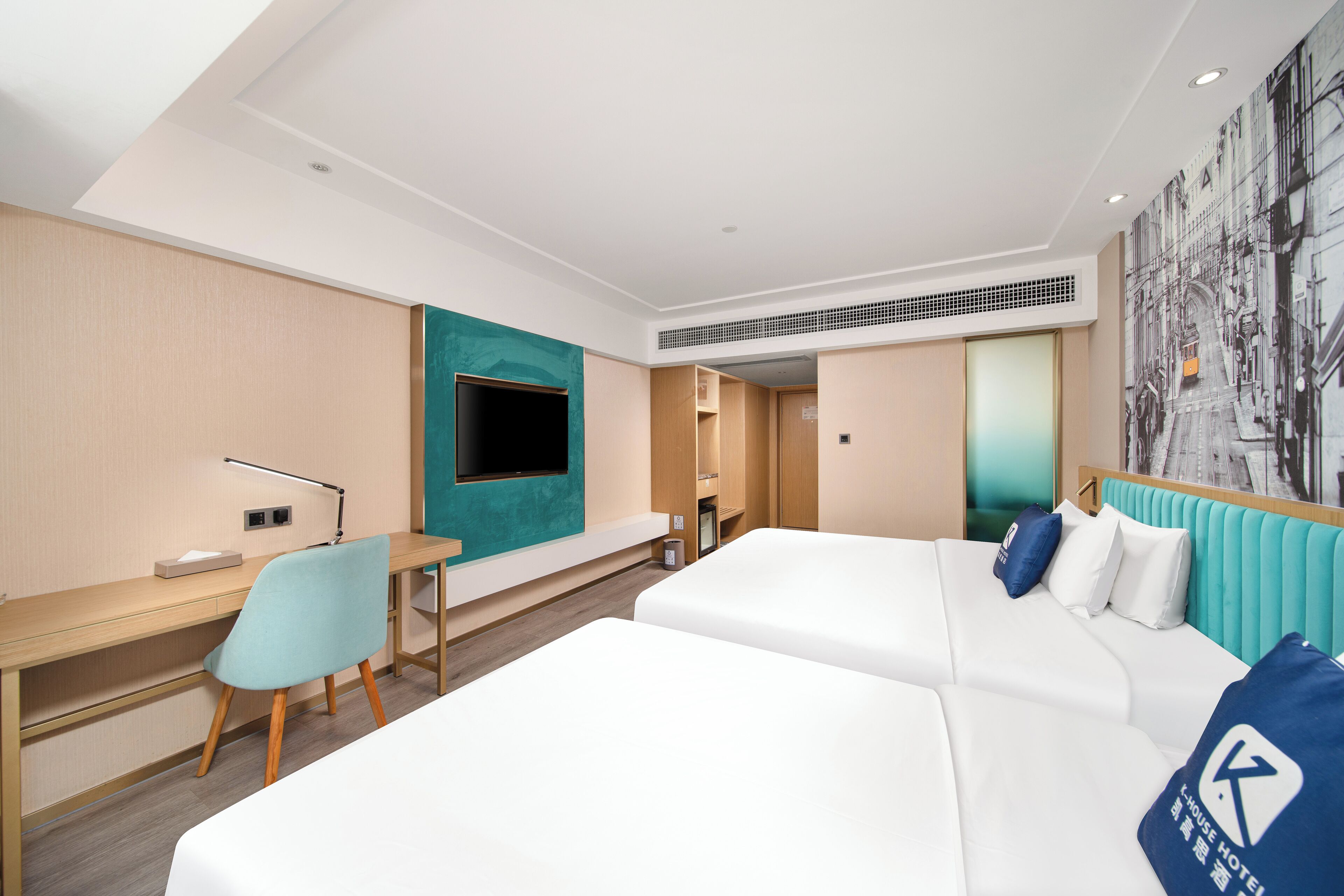 Una camera d'albergo con un letto, una scrivania, una sedia, una TV e un affresco sulla parete.