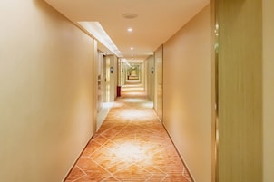 A long, well-lit hallway with a patterned floor, leading to multiple doors on either side.