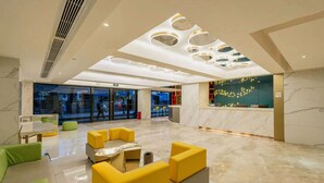 A spacious lobby with a marble floor, yellow and green seating, a reception desk, and a modern ceiling design. - K-house Hotel (Guangzhou)