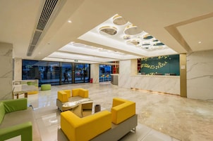 A spacious lobby with a marble floor, yellow and green seating, a reception desk, and a modern ceiling design.