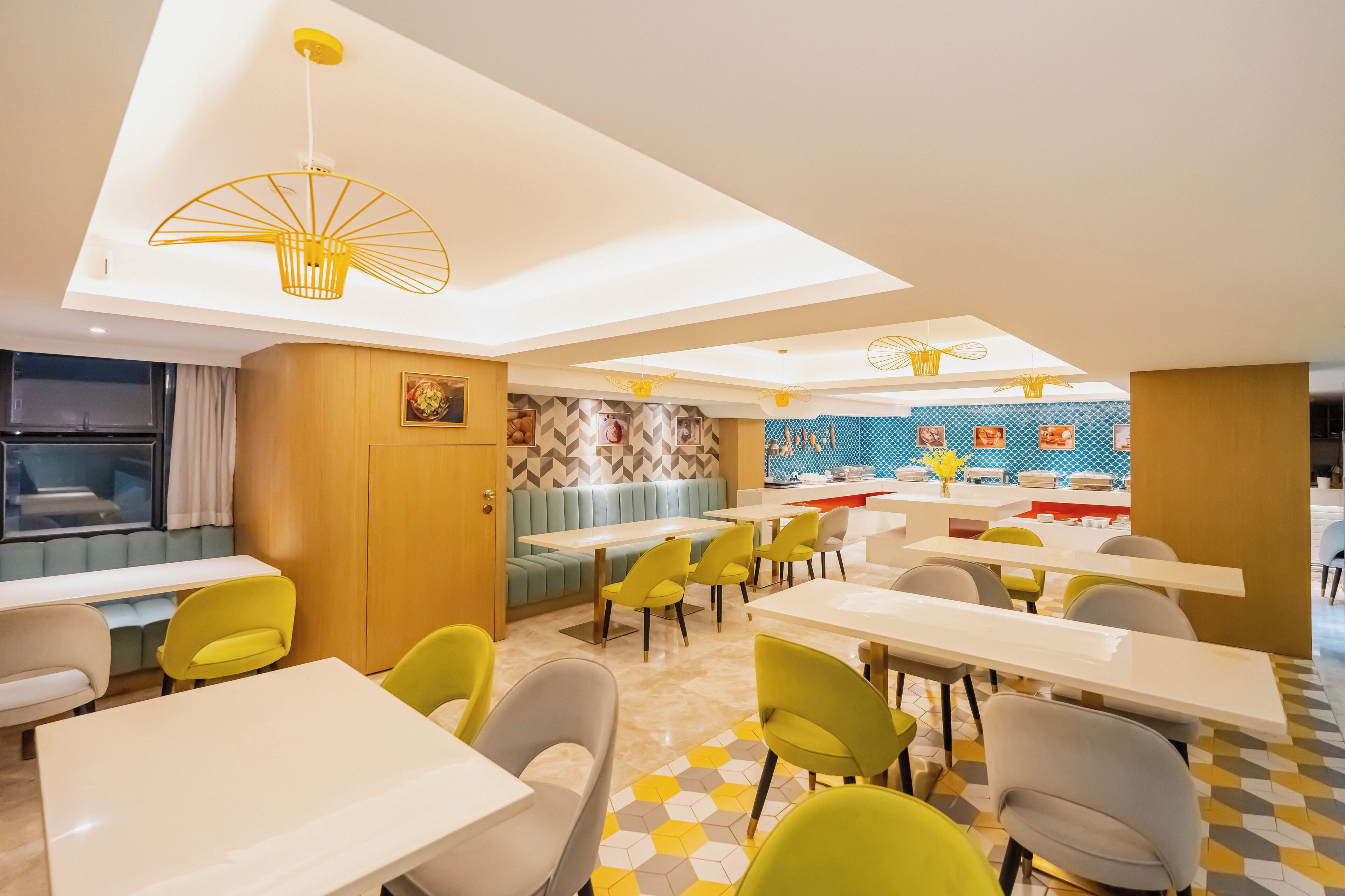 A modern dining area with yellow and grey chairs, white tables, and a blue and yellow patterned wall.