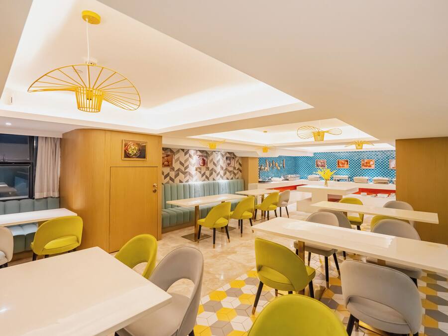 A modern dining area with yellow and grey chairs, white tables, and a blue and yellow patterned wall.