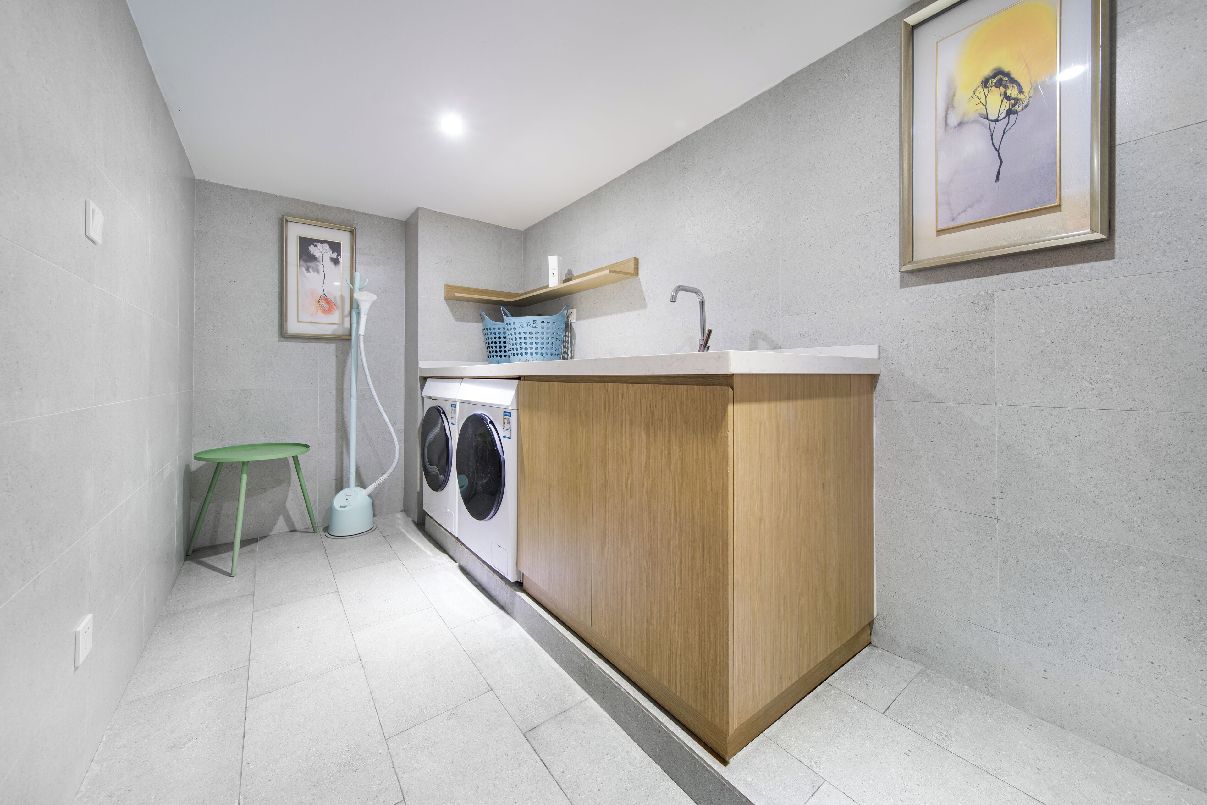 A compact kitchen with a washing machine, a sink, and a small stool.
