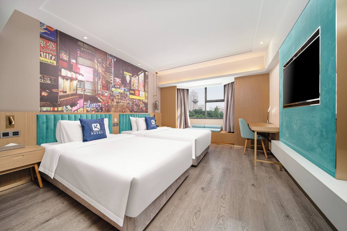 A hotel room with two beds, a desk, a TV, and a large cityscape mural on the wall.