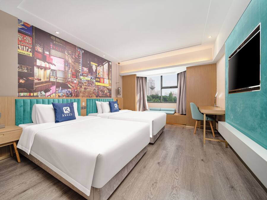 A hotel room with two beds, a desk, a TV, and a large cityscape mural on the wall.