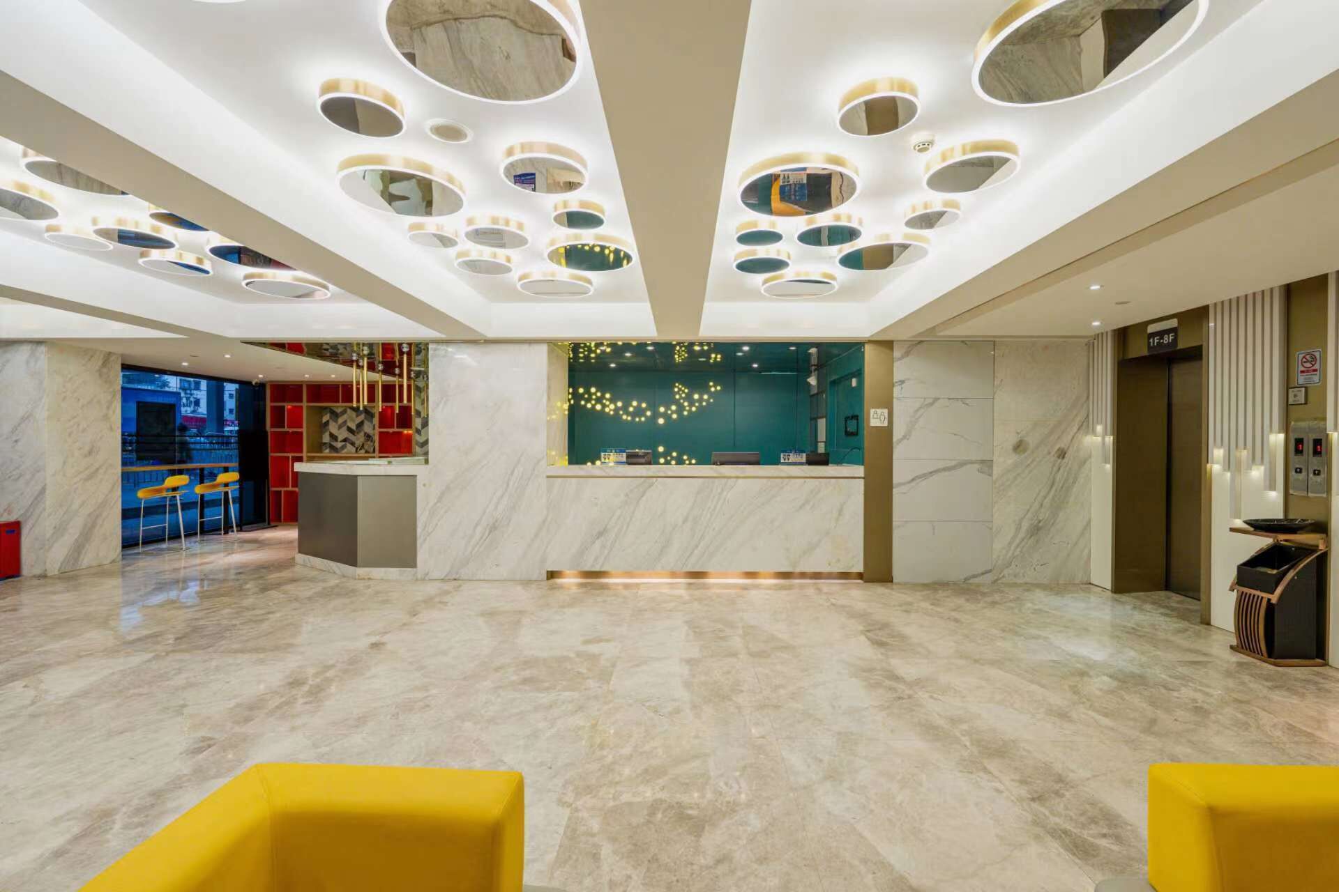 Eine moderne Hotelhalle mit Marmorboden, einer Rezeption und einer Bar mit gelben Stühlen.
